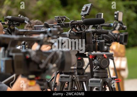 Videocamere professionali moderne posizionate su cavalletti sullo sfondo sfocato della natura durante le conferenze d'affari estive Foto Stock