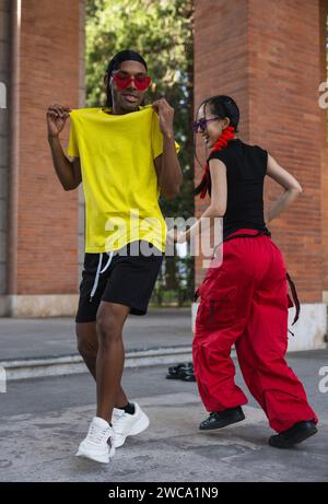 Una serie di immagini che catturano l'energia allegra di due compagni di danza in uno streetwear vivace, condividendo una danza e un caldo abbraccio sul marciapiede. Foto Stock