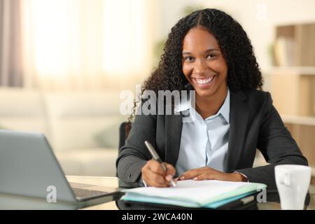 Felice telelavoratore nero firma modulo che ti guarda a casa Foto Stock