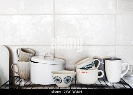Tazze grigie e bianche con cuori e scritte: Ti amo su uno scaffale della cucina sullo sfondo di una parete piastrellata grigia. Foto Stock