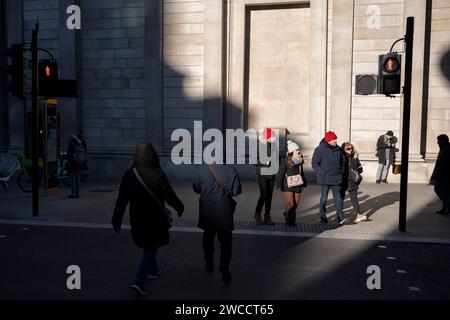 I lavoratori della città camminano attraverso la luce del sole invernale sotto le alte mura della Bank of England in Threadneedle Street, nella City di Londra, il quartiere finanziario della capitale, il 15 gennaio 2024, a Londra, Inghilterra. Foto Stock