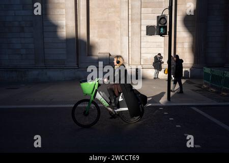 Una donna passa la sua Lime eBike attraverso la luce del sole invernale sotto le alte mura della Bank of England in Threadneedle Street, nella City of London, il quartiere finanziario della capitale, il 15 gennaio 2024, a Londra, in Inghilterra. Foto Stock