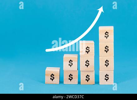 Immagine di blocchi di legno con segni di dollaro impilati in ordine crescente, che rappresentano la crescita finanziaria, con una freccia verso l'alto disegnata su sfondo blu. Foto Stock
