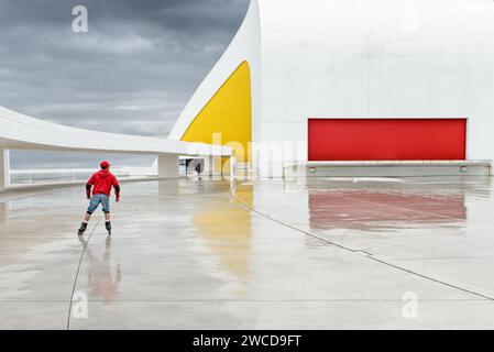 Uno skater con una giacca rossa al moderno Niemeyer Center in una giornata di pioggia, ad Aviles, Asturias, Spagna. Foto Stock