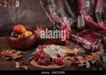 Piatto di formaggi servito con vino rosso, frutta autunnale e foglie secche Foto Stock