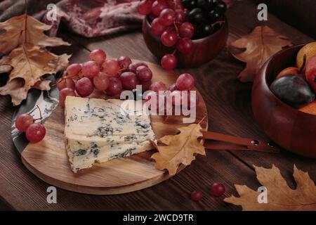 Piatto di formaggi servito con frutta autunnale e foglie secche Foto Stock