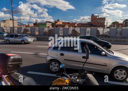 Complexo da Mare, un'enorme rete di favelas che si trova lungo la Linha Vermelha (linea rossa), l'autostrada principale dall'aeroporto internazionale di Rio de Janeiro al centro della città - dal 2010 la comunità è recintata dall'autostrada da enormi pannelli Perspex - una barriera di separazione lunga 7 km, alta 3 metri, decorata con graffit (in questa foto diverse rappresentazioni delle montagne di Rio) - le autorità affermano che fornisce una barriera acustica, la gente del posto lo descrive come un "muro della vergogna", un altro modo per nascondere i poveri. Foto Stock