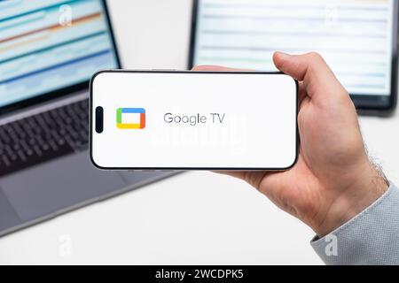 Logo Google TV dell'app sullo schermo del telefono cellulare tenuto dall'uomo davanti al laptop e al tablet, dicembre 2023, Praga, Repubblica Ceca Foto Stock