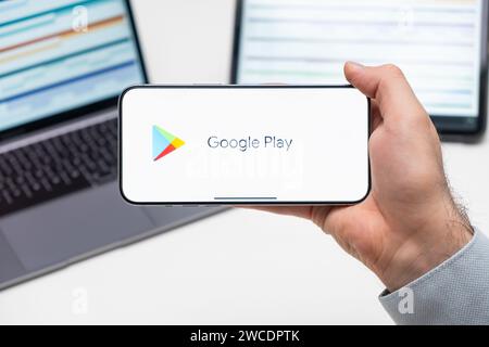 Logo Google Play dell'app sullo schermo del telefono cellulare tenuto dall'uomo davanti al laptop e al tablet, dicembre 2023, Praga, Repubblica Ceca Foto Stock