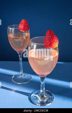 Due eleganti bicchieri ripieni di vino rosso sono posti uno accanto all'altro, accompagnati da un piatto di succulente fragole Foto Stock