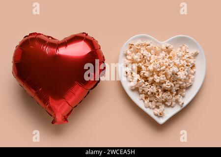 Piatto con popcorn e palloncino a forma di cuore su sfondo beige. Festa di San Valentino Foto Stock