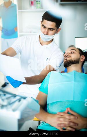 Un paziente su una sedia comunica con un dentista Foto Stock