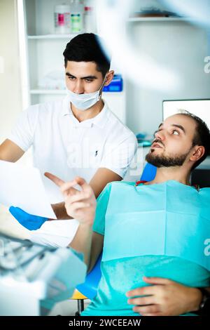 Un paziente su una sedia comunica con un dentista Foto Stock