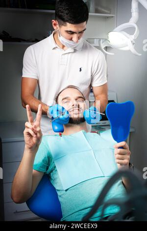 Un paziente al dentista guarda la telecamera con uno specchio Foto Stock