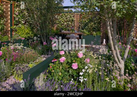 Un giardino interno circondato da scherma di salice e nocciole con un'area salotto e confini di erbacee perenni nella forma della terra Mental We Foto Stock