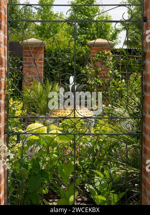 Una vista attraverso un cancello di ferro battuto verso una fontana circondata da una varietà di piante nell'Explore Charleston: Benvenuti al Charleston Garden Foto Stock