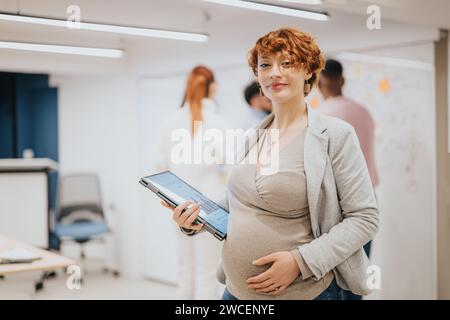 Donna d'affari che tiene in posa un notebook mentre i suoi compagni di squadra collaborano in ufficio. Foto Stock