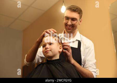 Parrucchiere professionale che lavora con il ragazzo in un salone di bellezza, con vista dall'angolo basso Foto Stock