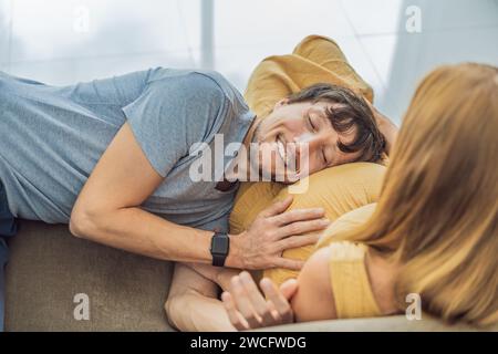 Momento tenero mentre il marito abbraccia amorevolmente la pancia di sua moglie incinta mentre sono seduti insieme sul divano, condividendo calore e anticipazione Foto Stock