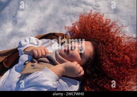 Vista dall'alto di una donna grassa dai capelli rossi sdraiata sulla neve. Foto Stock