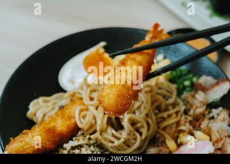 EBI Furai prelevato con bacchette nere in una piastra di Yaki Ramen. Autentici e tradizionali noodles giapponesi. Foto Stock