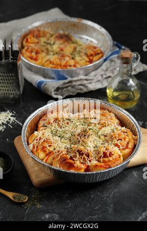 Pizza per pane a pasta spalmata con guarnizione di formaggio grattugiato su piastra di cottura in lamina di alluminio Foto Stock