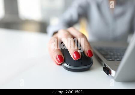 Donna con manicure rosso che tiene il mouse del computer vicino al closeup del laptop Foto Stock