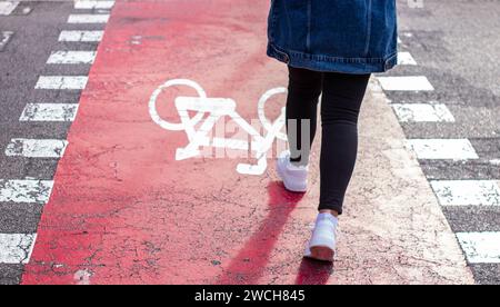 Le sneaker bianche con una giacca in denim attraversano i pedoni con una pista ciclabile. Cartello della bicicletta dipinto su asfalto. Foto Stock