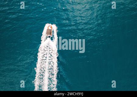 Il motoscafo naviga su un mare turchese, lasciandosi alle spalle un sentiero bianco schiumoso. Vista dall'alto Foto Stock