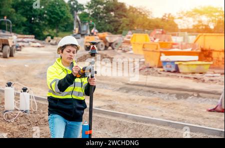 Geometra ingegnere del cantiere che lavora con apparecchiature EDM a stazione totale teodolite all'esterno di un cantiere edile Foto Stock