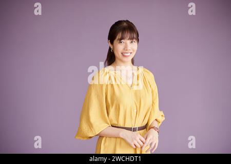 Ritratto in studio di una giovane donna d'affari sorridente in abito giallo su sfondo lilla Foto Stock