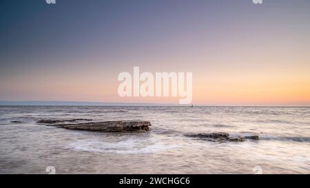 Costa rocciosa a Nash Point, Glamorgan, Galles meridionale. Tramonto sulla costa, lunga esposizione per attenuare i movimenti in mare. Foto Stock