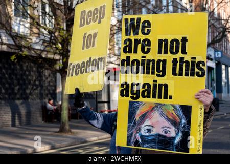 Manifestanti anti anti-vax con cartelli gialli con slogan anti-vaccino il primo giorno in cui l'ex primo ministro Boris Johnson ha partecipato all'inchiesta britannica Covid-19 il 6 dicembre 2023 a Londra, Regno Unito. L’inchiesta britannica sul COVID-19 è un’indagine pubblica indipendente sulla risposta del Regno Unito e sull’impatto della pandemia di coronavirus. I gruppi di esitazione del vaccino noti come anti-vaxxer o anti-vax, sono generalmente contro la vaccinazione. Foto Stock