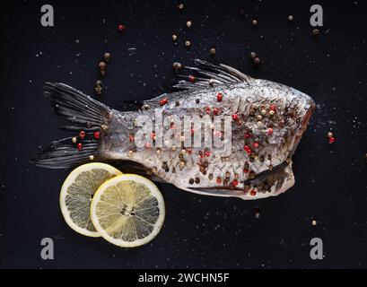 Carpa di crucian preparata per la cottura con pepe, sale e limoni su fondo nero. Foto Stock