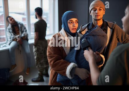 Riduci il ritratto di una coppia di rifugiati mediorientali con un bambino che parla con il microfono mentre fai un'intervista nel rifugio, nello spazio per le copie Foto Stock