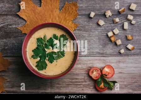 Zuppa vegetariana di crema di zucca con prezzemolo in una ciotola su un tavolo di legno con pomodori e cracker. Cibo tradizionale villaggio per Halloween. T Foto Stock