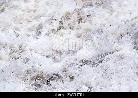 Acqua di mare schiumosa, onde che raggiungono la riva, schiuma di mare mista a ciottoli e sabbia, un movimento che descrive la fotografia, quasi audio. Foto Stock