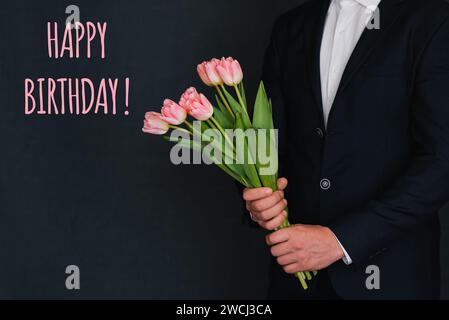 Bouquet di fiori rosa di tulipani nelle mani degli uomini in un completo. Biglietto d'auguri con l'iscrizione buon compleanno Foto Stock