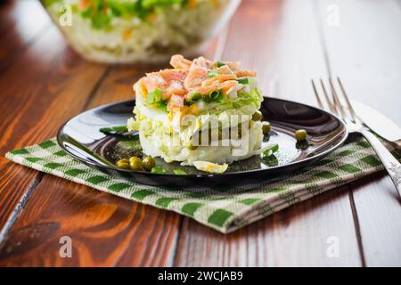 Insalata a strati di cavolo e altre verdure con pezzetti di pesce rosso in un piatto. Su un tavolo di legno. Foto Stock