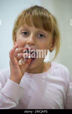 una bambina in pigiama tiene in mano una pillola da mangiare - sfondo sfocato. Foto Stock