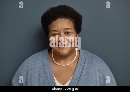 Ritratto frontale di una donna afroamericana matura che guarda la fotocamera e sorride su sfondo grigio Foto Stock