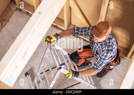 Operaio edile professionista arrampicata su una scala all'interno di una casa di recente sviluppo Foto Stock