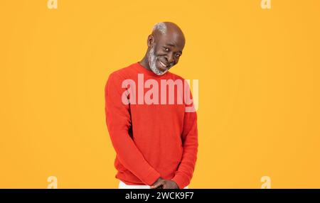 Uomo anziano sorridente e sicuro di sé con un maglione rosso e un cappello in piedi con le mani nelle tasche Foto Stock