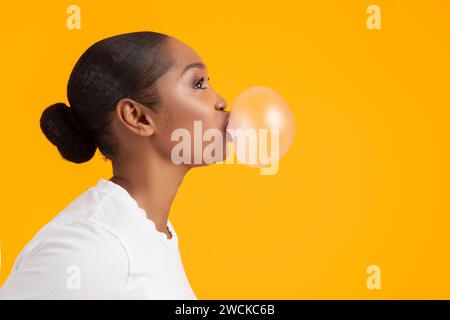 Ritratto laterale di una giovane donna nera che soffia bolla, studio Foto Stock