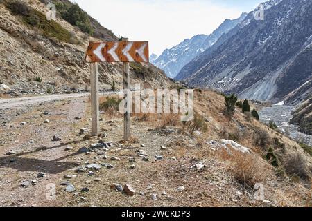 Vialetto pericoloso vicino alla scogliera. Cartello rosso con indicazione bianca a sinistra, girare le frecce sul lato della strada tra le montagne. Foto Stock