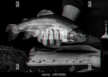 trota nelle mani di uno chef maschio in cucina. Grande pesce rosso fresco. Fotografia monocromatica in bianco e nero con effetto glitch 3D. Foto Stock