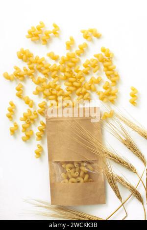 Sacchetto di carta kraft con spikelets di pasta e grano su sfondo bianco. Maccheroni a spirale di fusilli italiani. Ricette alimentari. Mangiare sano. Vista dall'alto, f Foto Stock