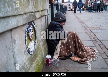 Eton, Windsor, Regno Unito. 16 gennaio 2024. Un senzatetto siede tristemente sul Windsor Bridge a Windsor, nel Berkshire, con una coperta che copre le ginocchia in una giornata fredda e gelida. L'uomo chiedeva ai passanti se potevano risparmiare qualche cambiamento. Il protocollo di emergenza tempo grave è attualmente in vigore nel Royal Borough di Windsor & Maidenhead il che significa che le persone senza tetto possono ottenere un alloggio temporaneo per la notte. Credito: Maureen McLean/Alamy Live News Foto Stock