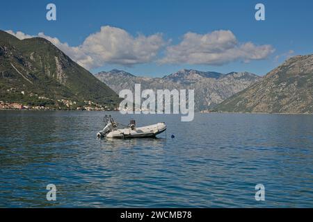 Un gommone con motore fuoribordo galleggia tranquillamente sulle tranquille acque della Baia di Cattaro, circondato dal suggestivo paesaggio montuoso di Mon Foto Stock