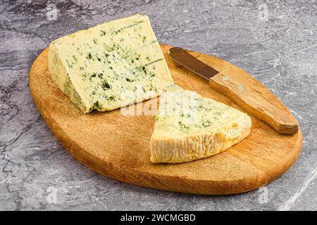 Una singola fetta di formaggio su un tagliere di legno rustico, accompagnato da un coltello e un tagliere Foto Stock